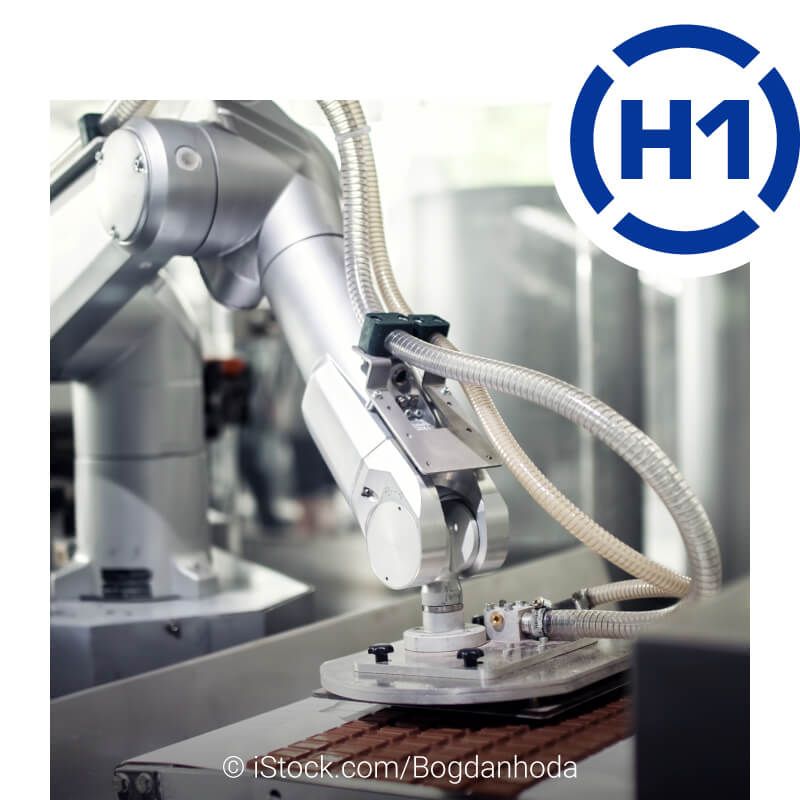 Ein Industrieroboter mit Schläuchen und einer pneumatischen Vorrichtung in der Lebensmittelproduktion. Er greift auf ein Förderband und positioniert die Schokoladentafel. Rechts oben ist das H1-Logo abgebildet.