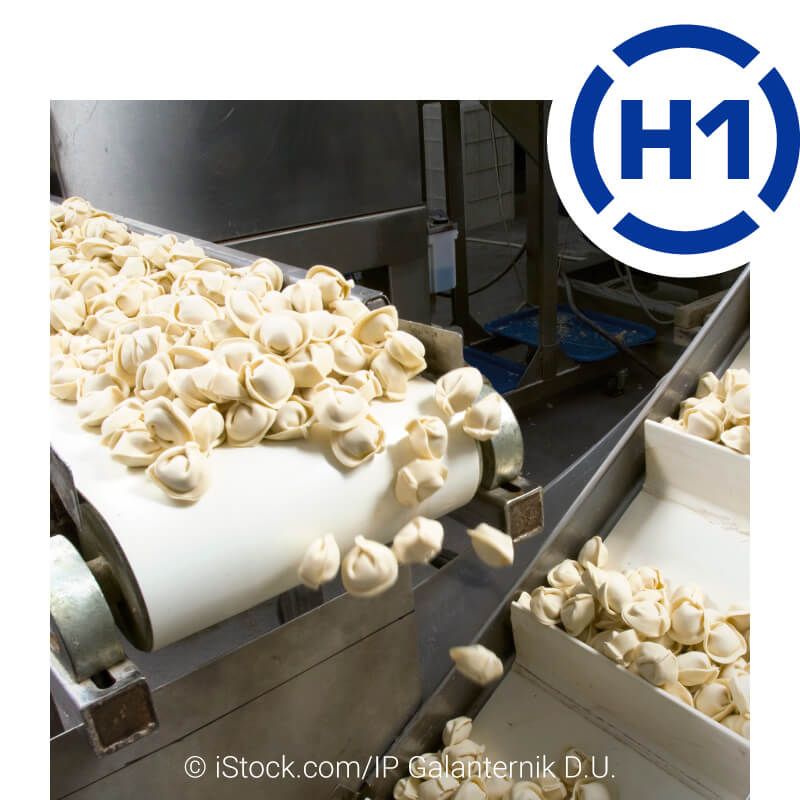 Detailansicht in einer Lebensmittel-Verpackungsanlage. Von einem Förderband werden rohe Tortelloni in eine Portioniermaschine gegeben. Rechts oben ist das H1-Logo abgebildet.